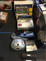 Photo showing boxed DirecTV Blue DVR Ultraslim, Philips sound system box, silver portable boombox/recorder, and other electronics arranged on carpeted floor