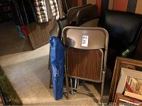 Photo showing stacked metal folding chairs with wood-patterned seats and backs, along with a blue canvas lawn chair bag.