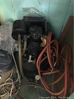 Full view of the black air compressor showing the motor, air filter, connected red hose and surrounding area.