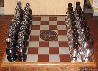Chess board with chess pieces arranged for a game, pieces made of dark and clear glass with metallic tops.