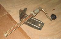 Full view of vintage counter mount can opener with silver metal body and wooden handle, placed on a wooden surface.