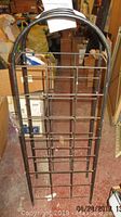 Full view of metal wine rack in storage setting showing arched top, grid design and some surface rust