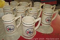 Ten white ceramic steins with Philadelphia 76ers logos visible on the front, arranged in two rows on a table. Red and blue colors are prominent in logos and trim.
