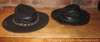 Two leather cowboy hats side by side on wooden surface, brown Minnetonka hat on left, black unknown maker hat on right.