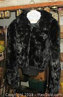 Front view of black rabbit fur jacket hanging on white hanger showing texture, length, and ribbed cuffs.