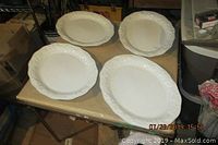 Four white ceramic oval serving platters with decorative embossed edges laid on table, front view