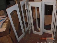Pair of white wooden shutters standing open, showing two different sized glass panel openings on each door.