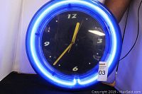 Front view of round blue neon clock showing clock face and neon light ring illuminated.