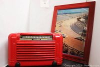 Photo showing the red Motorola radio with metal casing in front of the glass framed beach car race picture.