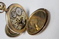 Antique 10ct gold pocket watch showing the back case open revealing the detailed inner mechanical movement with gears and jewels visible.