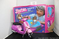 Photo showing pink Barbie bubbling spa with original box in the background and pink Barbie scooter in front