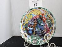 Front of a limited edition Wizard of Oz fine china musical plate titled "The Merry Old Land of Oz." Shows detailed artwork of characters from the movie with colorful background and holly-decorated rim.