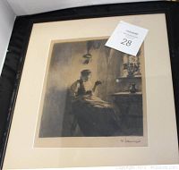 Framed chromo lithograph showing a seated woman embroidering near a window with a vase on the sill, signed by artist in bottom right.