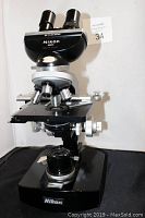 Front and side angled view of Nikon microscope showing binocular eyepiece, objectives, mechanical stage and focusing knobs.