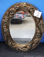 Front view of the antique oval mirror showing carved decorative frame and reflective glass surface with some visible chipping near the bottom.
