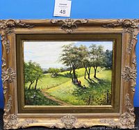 Front of ornate framed oil painting depicting countryside scene, trees, people, dirt path, and animals