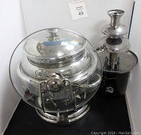 Photo showing the large soup terrine with lid and the chocolate tower fountain placed side by side on a black surface.