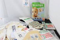 Photo showing a Photo Stamps gift card booklet with baby on the cover, loose and uncut stamps on envelopes, and some small booklets and papers scattered around.