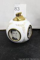 Front view of the round porcelain table lighter showing gold leaf design and two photo slots with portraits inside.