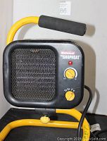 Front view of black Envirotech ShopHeat portable electric heater with yellow frame, control knobs, and indicator light visible