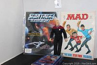Photo showing Star Trek Official Fan Club Magazine, MAD Magazine with Star Trek musical cover, Captain Picard action figure, and Star Trek IV VHS tape.