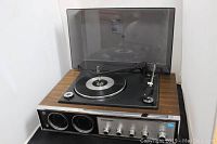 Front side view of the Panasonic record player showing the turntable with the tonearm and platter under a closed tinted dust cover. Unit has wood grain finish sides and top.