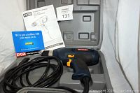 Corded Ryobi 3/8 inch drill with black and blue body, ergonomic grip, placed inside compartment of gray molded plastic carrying case along with owner's manual and registration card