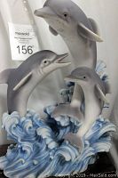 Front and side views of the ceramic dolphins statue showing the three dolphins in motion with detailed blue and white ocean waves base.