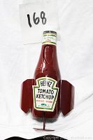 Red Heinz ketchup bottle shaped like flying rocket with wings and Heinz Tomato Ketchup label on front against white background.