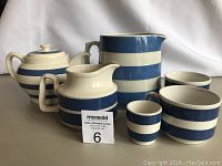 Overview photo showing six blue and white horizontally striped stoneware kitchenware items including a teapot, two pitchers, two bowls, and one small cup.