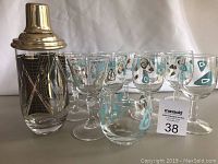 Full set showing vintage martini shaker with gold-toned lid and geometric black and gold design, alongside multiple stemmed glasses and one tumbler with blue and gold abstract patterns