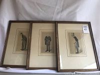 Three framed caricature prints arranged side by side showing wood frames and visible cardboard mats inside frames.