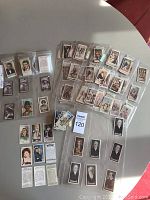 Overview of multiple cigarette card sets laid out on table, individually sleeved and grouped by series.