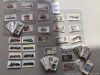 Photo showing groups of vintage cigarette cards mostly in protective sleeves laid out flat, featuring trains, industrial machines, and nature themes.