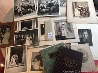 Overview of various framed and mounted black and white family photos including wedding portraits, baby pictures, and formal group shots accompanied by vintage book