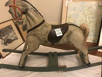 Side view of folk-art wooden rocking horse with visible age wear and damage to rocker base and rear left leg.