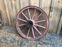 Front view of the antique red painted wooden wagon wheel with black metal hub center and 12 spokes.