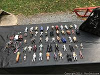 Wide view of the Star Wars figures spread out on a black cloth with the Darth Vader carrying case to the side, showing an assortment of around 55 figures and accessories including weapons and a Yoda PEZ dispenser.