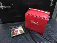 Full view of the red Coca-Cola cooler and vintage Santa Coca-Cola tray on black background.