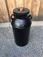 Front angle view showing the full large black antique milk can with wooden lid and both handles visible.