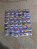 Overview photo showing 37 sealed Hot Wheels cars in blister packs arranged in rows on carpeted floor.