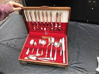 Full view of open wooden knife and flatware box with 54 pieces of Oneida Community silverware inside, showing various types of forks, spoons, and knives arranged in slots lined with red velvet and white satin.