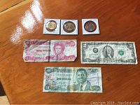 Display of three American 1 dollar coins in holders, two Bahama banknotes and one US 2 dollar bill on wooden surface