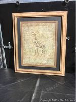 Full view of the framed giraffe picture showing the wooden frame, mat, and the artwork behind glass.