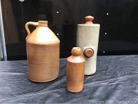 Three stoneware crocks on a black surface showing front view including hot water crock and two jugs.