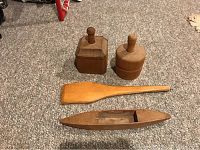Four antique wooden kitchen items on carpet: two butter stamps, flat spatula, and hollowed wooden tool.