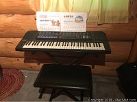 Full view of Casio keyboard set up with black vinyl seat and X-stand, beginner music book open on keyboard