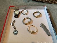 Overview of all items including four watches, pocket knife, charm bracelet, and belt watch all placed in a tray.