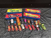 Top-down photo showing four vintage Hot Wheels cases and 21 vintage Hot Wheels and Matchbox cars arranged on a dark surface.