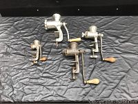 Four antique manual meat grinders lined up showing front views and handles.